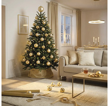Feestelijk versierde kunstkerstboom met gouden kerstballen en lichtjes in een lichte woonkamer met bank en salontafel.