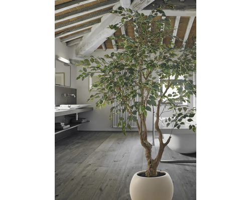 Grote kunstboom in een pot in een moderne badkamer met houten vloer, vrijstaand bad en zichtbare plafondbalken.