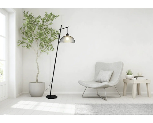 Moderne booglamp van zwart metaal met een kap van gaas in een lichte woonkamer met fauteuil en kamerplant.