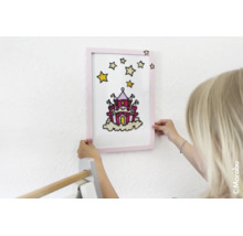 Kind houdt een ingelijst schilderij met een kasteel en sterren tegen de muur.
