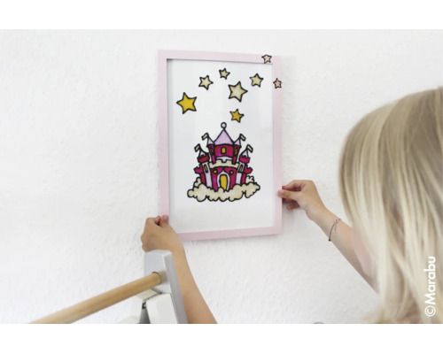 Kind houdt een ingelijst schilderij met een kasteel en sterren tegen de muur.