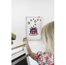 Een kind houdt een met glasverf gemaakte afbeelding van een kasteel in een lijst tegen de muur. Marabu Logo.