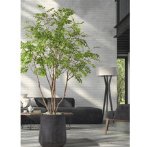 Grote kunstboom in een donkere plantenbak in een moderne woonkamer met een witte bakstenen muur, een donkere bank en een vloerlamp.