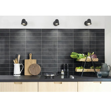 Georganiseerde moderne keuken met donkere rechthoekige wandtegels, lichte houten kasten, houten snijplanken en een kookplaat.