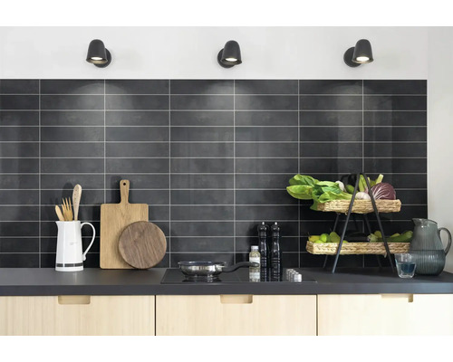 Georganiseerde moderne keuken met donkere rechthoekige wandtegels, lichte houten kasten, houten snijplanken en een kookplaat.
