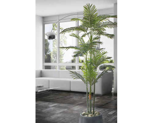 Kunstpalm in pot in een lichte, moderne woonkamer met witte bank, glazen tafel en een booglamp voor een raam.