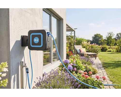 Wandslangenbox van for.q aan een buitenmuur in een verzorgde tuin met bloembedden, gazon en een ligstoel.