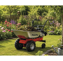 Gemotoriseerde kruiwagen PowerPac met metalen bak gevuld met tuinafval op een gazon in een lichte, bloeiende tuin.