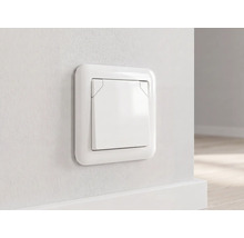Wit inbouwstopcontact met klapdeksel, gemonteerd op een muur boven een plint.