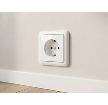 Wit geaard stopcontact met afgerond frame gemonteerd op een muur boven een plint.