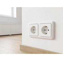 Dubbel geaard stopcontact horizontaal gemonteerd op een muur boven een houten plint in een lichte, moderne kamer.