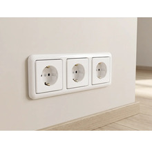 Witte 3-voudige geaarde wandcontactdoos met afdekraam, horizontaal gemonteerd op een muur boven een plint in houtoptiek.