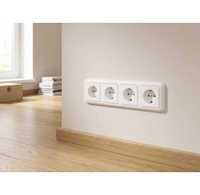 Viervoudig stopcontact op een lichte muur boven een houten plint in een lichte, modern ingerichte kamer.