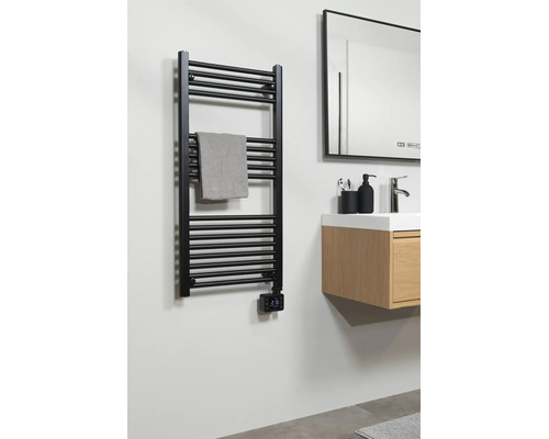 Zwarte handdoekradiator met digitale thermostaat in de badkamer naast een houten wastafelmeubel met wasbak en spiegel.