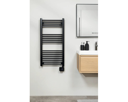 Moderne elektrische handdoekradiator in zwart met digitale thermostaat, gemonteerd naast een houten wastafelmeubel in een lichte badkamer.