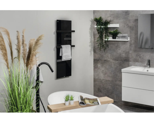 Moderne badkamer met zwarte glazen handdoekradiator, vrijstaand bad en wit wastafelmeubel tegen een grijze wand met steenlook.