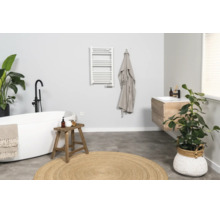 Moderne, lichte badkamer met vrijstaand bad, houten wastafelmeubel, witte handdoekradiator en rond jute vloerkleed.