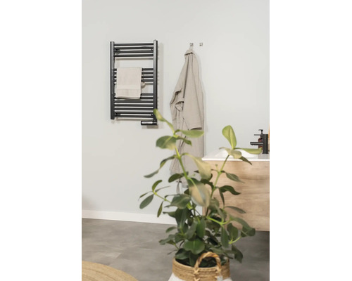 Zwarte elektrische handdoekradiator in een moderne badkamer met handdoek, badjas en wastafel.