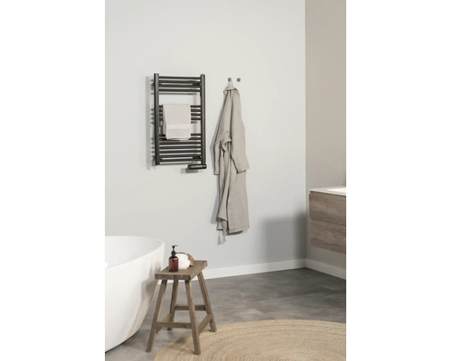 Moderne, lichte badkamer met een zwarte handdoekradiator aan de muur, een witte badkuip, een houten krukje en een badjas.