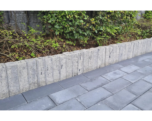 Betonnen palissaden als border tussen een bestraat pad en een tuin met struiken.