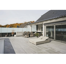 Modern terras met lichtgrijze vloertegels, lichte rotan tuinmeubelen, ligbedden en glazen afscheiding.