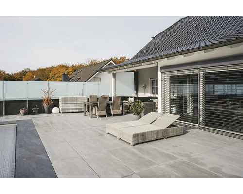 Modern terras met lichtgrijze vloertegels, lichte rotan tuinmeubelen, ligbedden en glazen afscheiding.