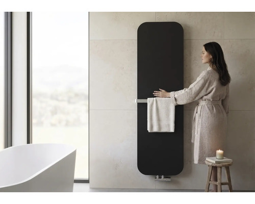 Verticale badkamerradiator met handdoekhouder in een moderne badkamer met vrijstaand bad en vrouw in badjas.