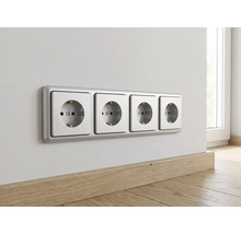 Horizontale 4-voudige wandcontactdoos met randaarde en zilverkleurig frame op een muur boven een houten plint in een lichte kamer.