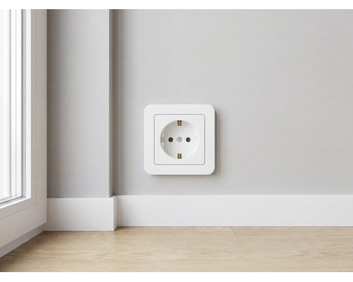 Moderne witte kunststof wandcontactdoos met randaarde aan een muur boven een witte plint en lichte houten vloer in een lichte kamer.