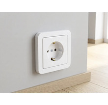 Wit geaard stopcontact met een afgerond frame gemonteerd op een muur boven een houten plint.