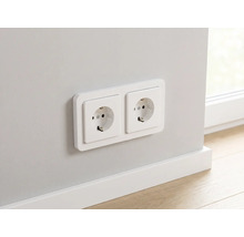 Dubbele wandcontactdoos met randaarde gemonteerd op een muur boven een witte plint.