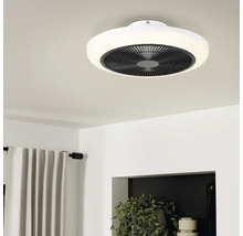 Moderne, ronde plafondventilator met LED-lichtring aan een plafond in een lichte, opgeruimde kamer met gordijnen en kamerplanten.