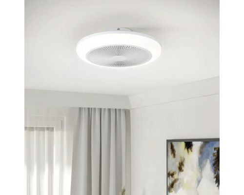 Moderne ronde plafondventilator met geïntegreerde LED-lichtring, gemonteerd aan een wit plafond in een lichte kamer.
