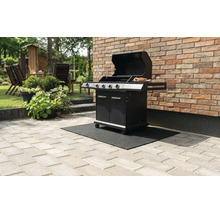 Zwarte gasbarbecue met open deksel op een zwarte barbecue vloermat op een stenen terras naast een bakstenen muur.