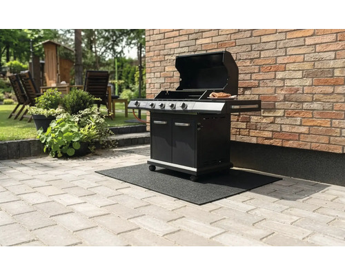 Zwarte gasbarbecue met open deksel op een zwarte barbecue vloermat op een stenen terras naast een bakstenen muur.
