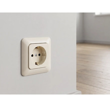 Schuko stopcontact in crèmewit, gemonteerd op een wand in een lichte kamer met houten vloer.