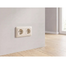 Dubbele wandcontactdoos gemonteerd op een lichte muur boven een houten vloer in een moderne, lichte kamer.