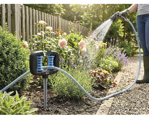 Slanggeleider in een bloembed met een tuinslang en een persoon die op de achtergrond planten water geeft.