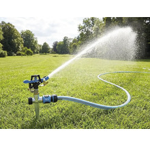 Impulssproeier met grondpen op een gazon, aangesloten op een tuinslang, sproeit een brede waterstraal voor tuinbesproeiing.