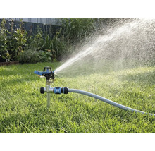Pulsatiessproeier met grondpen op het gazon, aangesloten op een tuinslang, sproeit water in een brede straal.