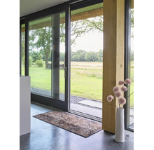 Modern interieur met grote glazen schuifdeur naar de tuin, decoratieve deurmat op betonnen vloer en houten steunbalk.