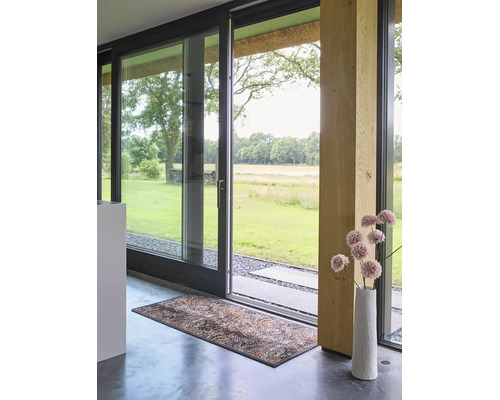 Modern interieur met grote glazen schuifdeur naar de tuin, decoratieve deurmat op betonnen vloer en houten steunbalk.