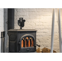Zwarte gietijzeren houtkachel met brandend vuur, een kachelventilator bovenop en haardstel voor een witte bakstenen muur.