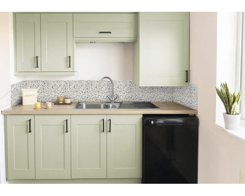 Moderne keuken met saliegroene kasten, zwarte handgrepen, keukenachterwand in terrazzo-look, roestvrijstalen spoelbak en werkblad in houtlook.