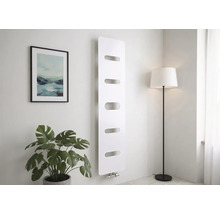 Moderne verticale radiator in wit met vijf horizontale uitsparingen, gemonteerd op een wand in een lichte kamer met een plant en vloerlamp.
