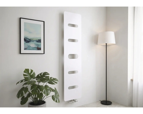 Moderne verticale radiator in wit met vijf horizontale uitsparingen, gemonteerd op een wand in een lichte kamer met een plant en vloerlamp.