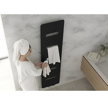 Zwarte handdoekradiator in een moderne badkamer met marmeren wand. Een vrouw in een badjas hangt een handdoek op.