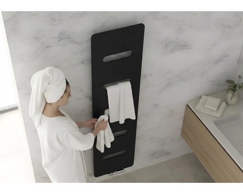 Zwarte handdoekradiator in een moderne badkamer met marmeren wand. Een vrouw in een badjas hangt een handdoek op.