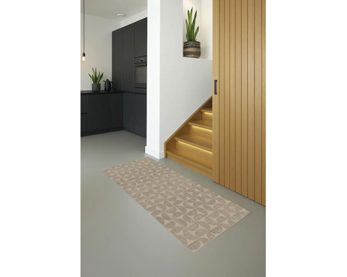 Moderne woonruimte met een vloerkleed met geometrisch patroon, grijze vloer, zwarte keuken en verlichte houten trap.