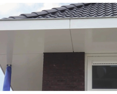 Witte dakoverstekbekleding van gladde panelen bij een dakrand met donkere dakpannen en een bakstenen gevel.